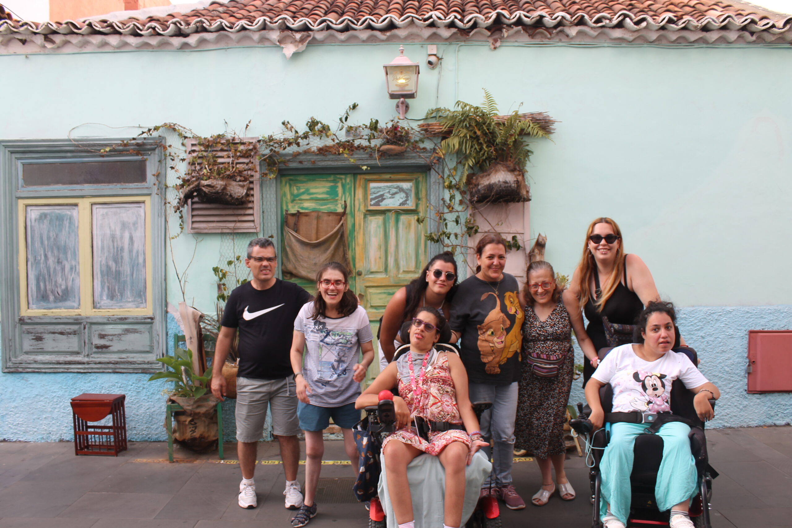Grupo de personas de Asprona en la calle, frente a una casa, posando sonrientes para una foto mientras dan un paseo