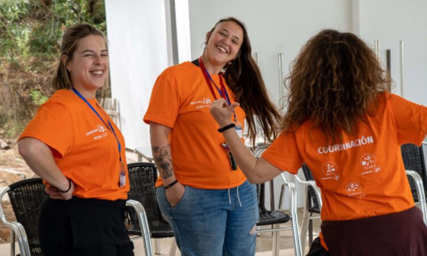 Tres personas de Asprona, dos sonriendo y una de espaldas, señalando con los pulgares su camiseta con la palabra 'coordinación'