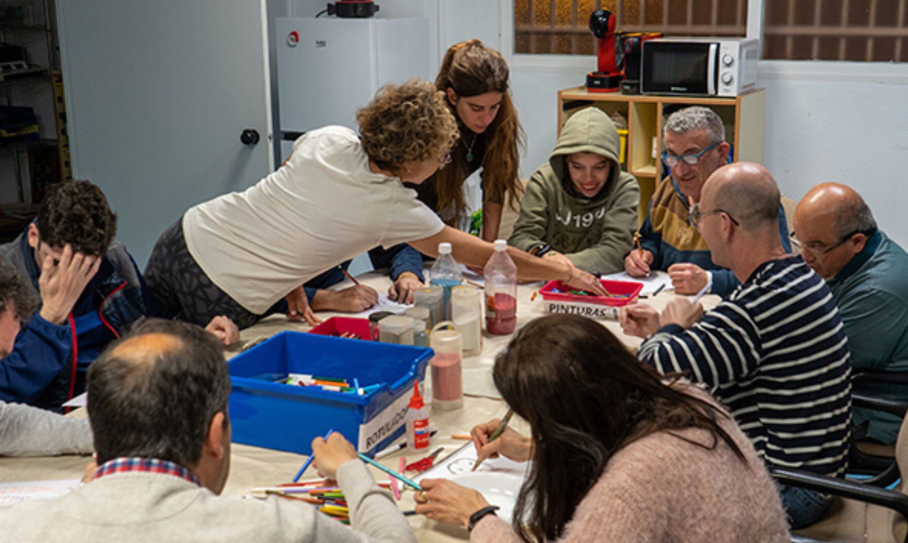 Grupo de personas sentadas alrededor de una mesa en un espacio cerrado, participando en una actividad de pintura