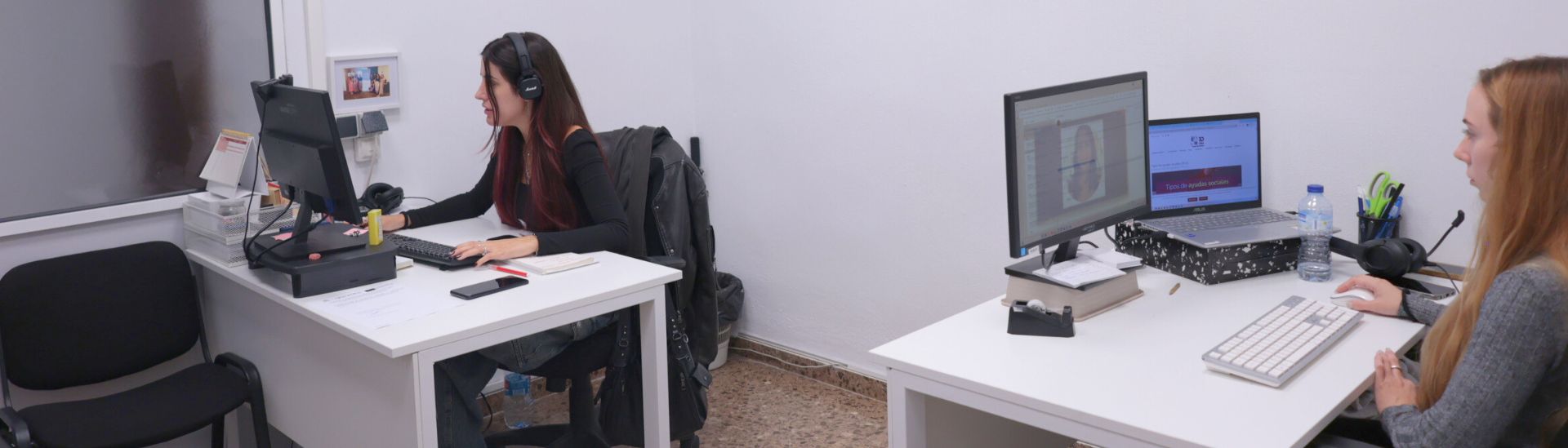 Dos personas trabajando en ordenadores en dos escritorios de una oficina, cada una en su espacio